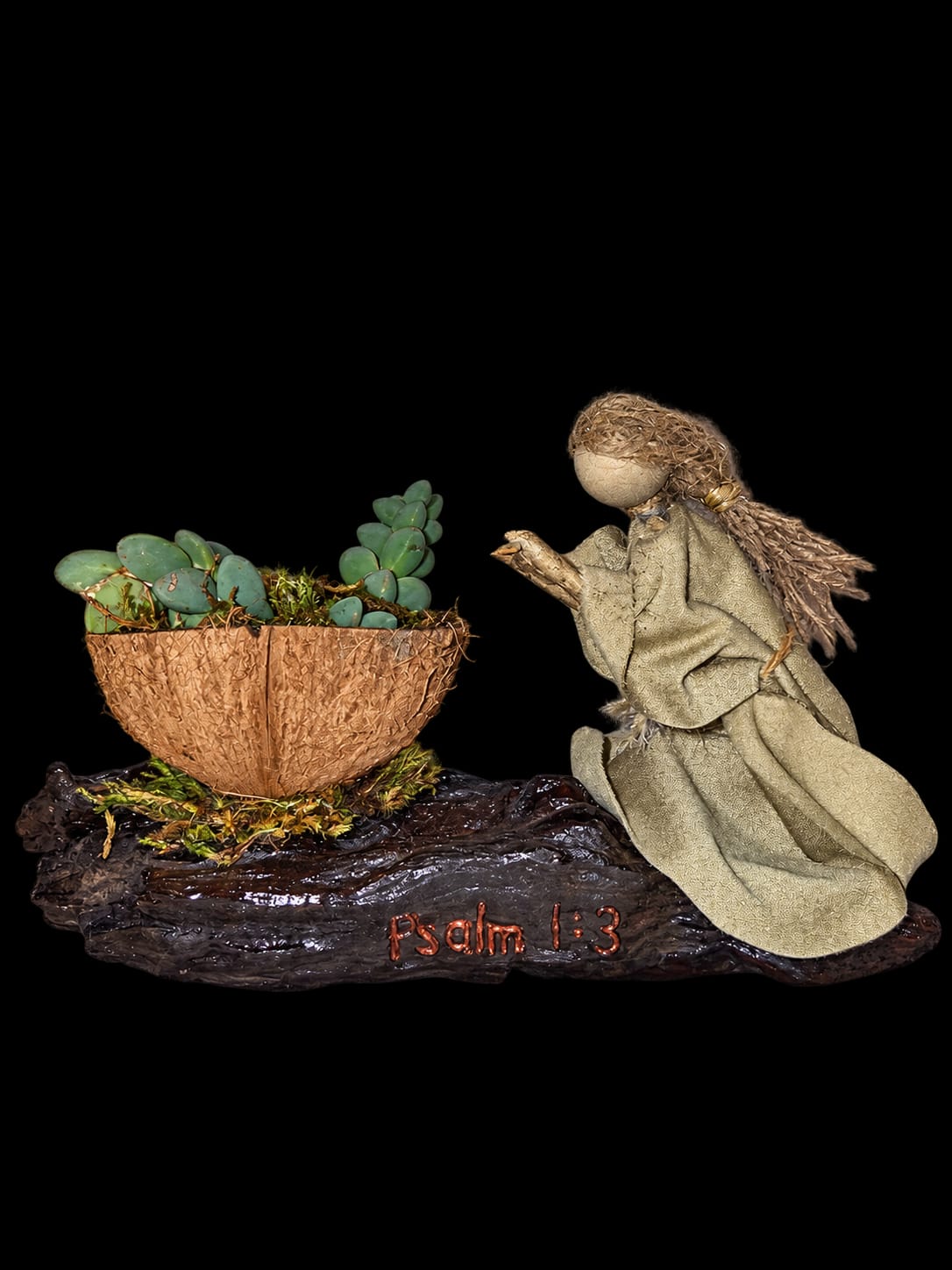 Kneeling handmade figure beside greenery on a wooden base inscribed Psalm 1:3